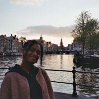 This is a picture of me in the the center of Amsterdam standing in front of a canal with some buildings in the background.