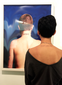 This photograph is letting the viewers be the judge of the artwork. The portrait that the figure is looking at is a nude woman with a “DYKE” printed tattoo on the back of her neck. The figure is positioned next to the portrait because they both resemble each other with their short hair styles. On the figure’s back of the neck, it says “ INSERT LABEL HERE”. She let’s the audience fill in the unknown spaces to form her identity. 